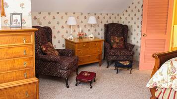 A room with a wooden dresser, two patterned armchairs, a wooden cabinet, and a small red ottoman.