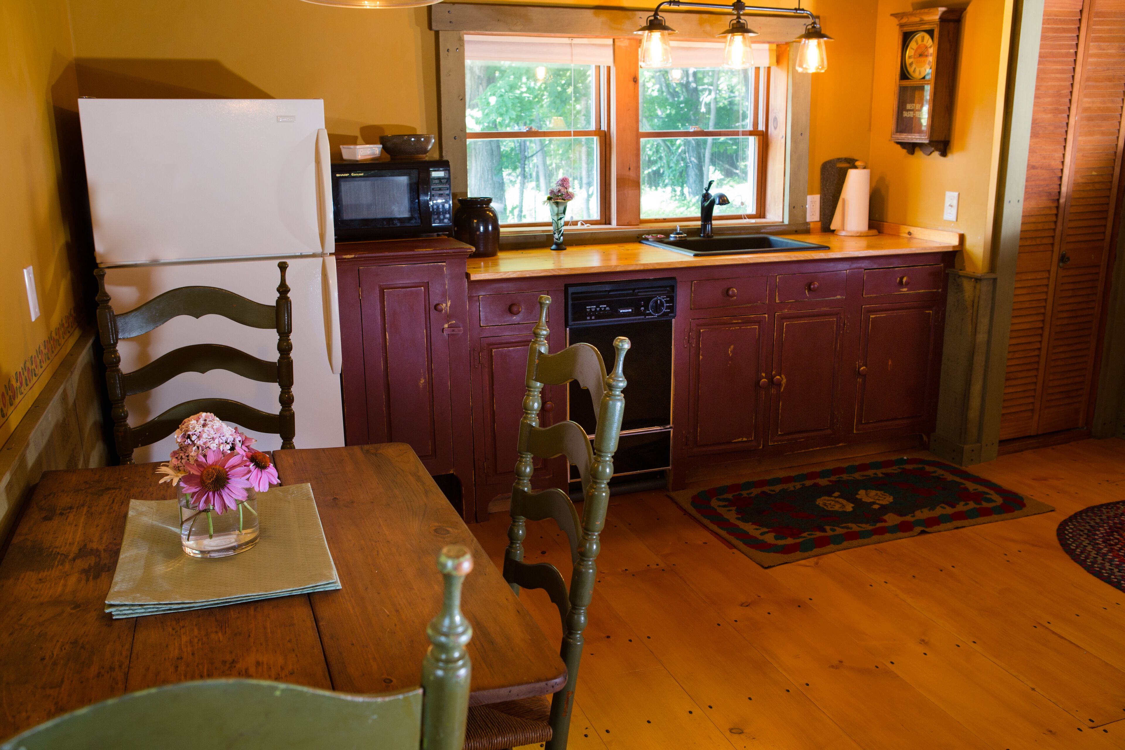 A kitchen with wooden cabinets, a refrigerator, a microwave, a sink, and a window with a view of trees.