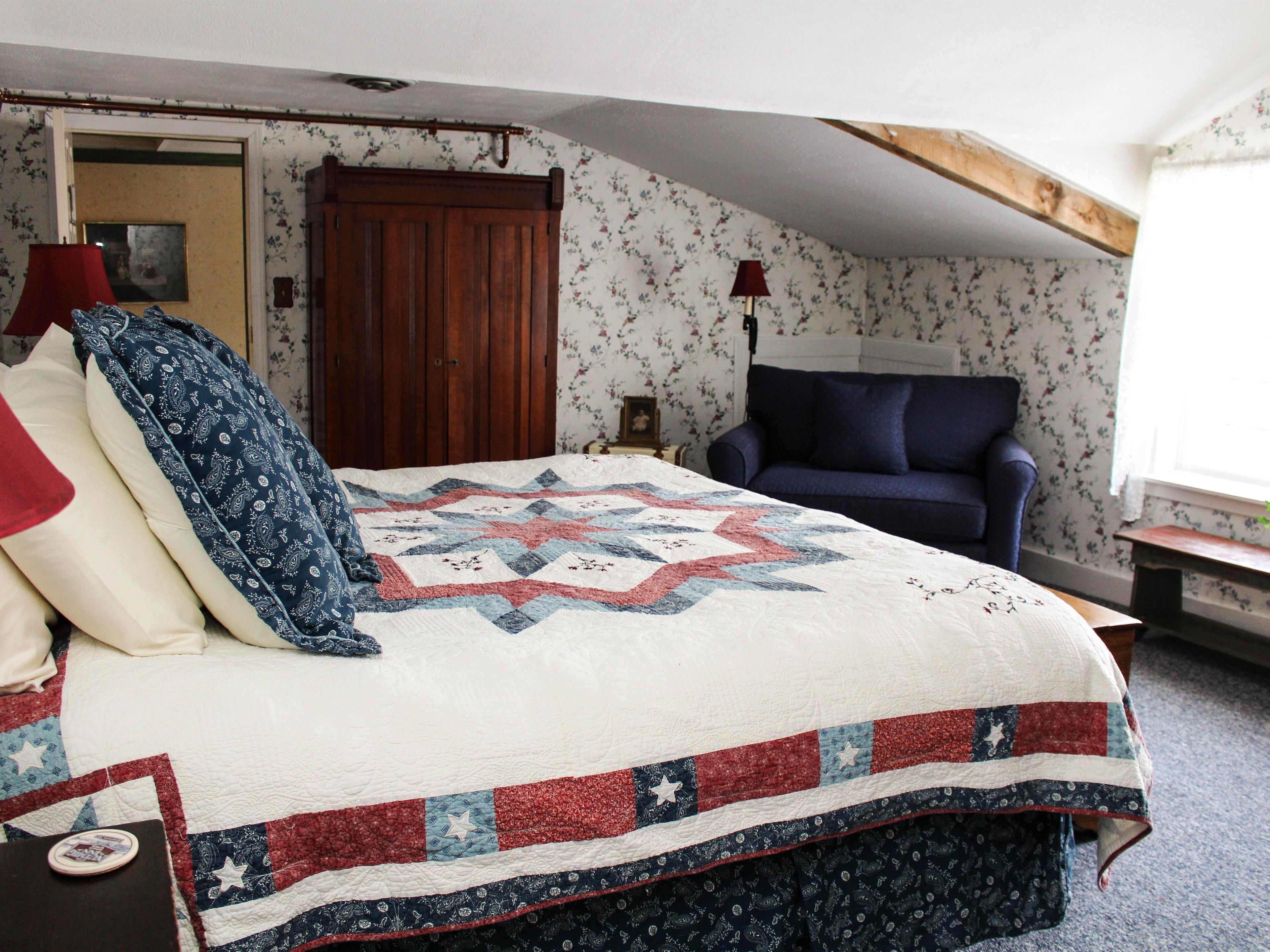 Un dormitorio con cama, sofá azul, puerta de madera y papel tapiz floral.