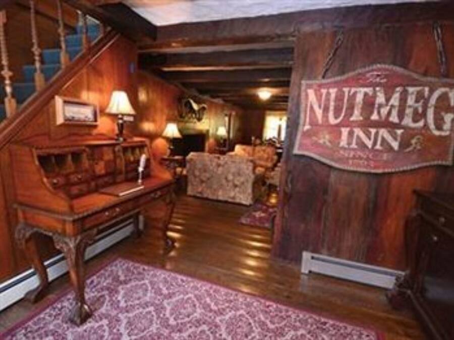 Interior de madera con una escalera, un letrero que dice 'The Nutmeg Inn' y una alfombra estampada.