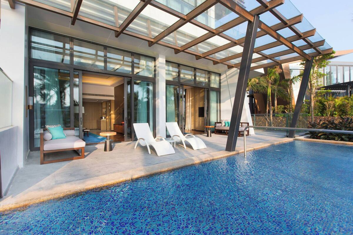 Un espace piscine moderne avec des murs en verre, des chaises longues et une vue dégagée sur la piscine.