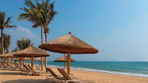 A beach with thatched umbrellas and lounge chairs.