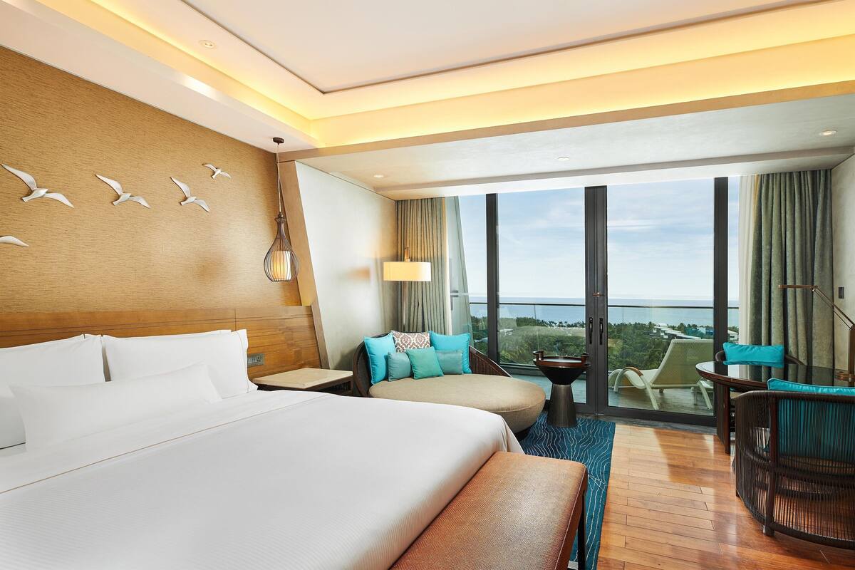 Une chambre d’hôtel dotée d’un grand lit, d’un coin salon avec vue et d’un balcon agrémenté d’une table et de chaises.