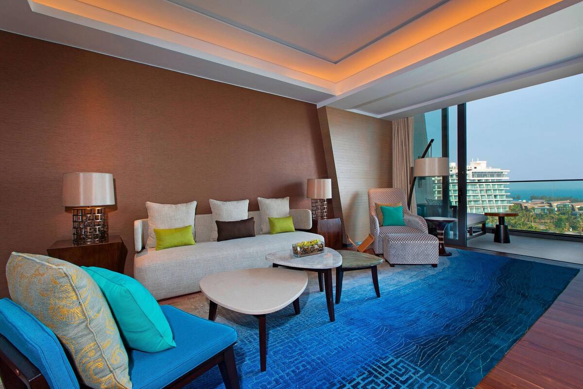 Une chambre d’hôtel moderne dotée d’un grand lit, d’un canapé, de deux fauteuils, d’une table basse et offrant une vue sur la ville.