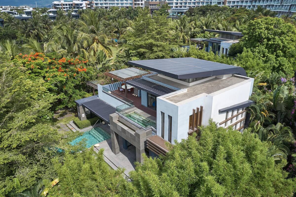 Une maison moderne dotée d’une piscine sur le toit, entourée d’une végétation luxuriante et de palmiers.