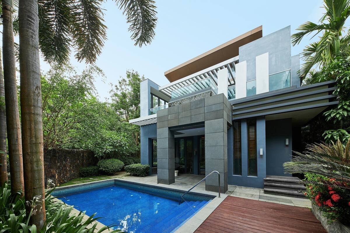 Une maison moderne avec une piscine, entourée d’une végétation luxuriante et de palmiers.
