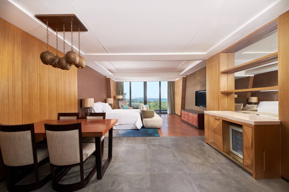 Une chambre d’hôtel moderne dotée d’un coin repas, d’un canapé-lit, d’une télévision et offrant une vue sur l’océan.