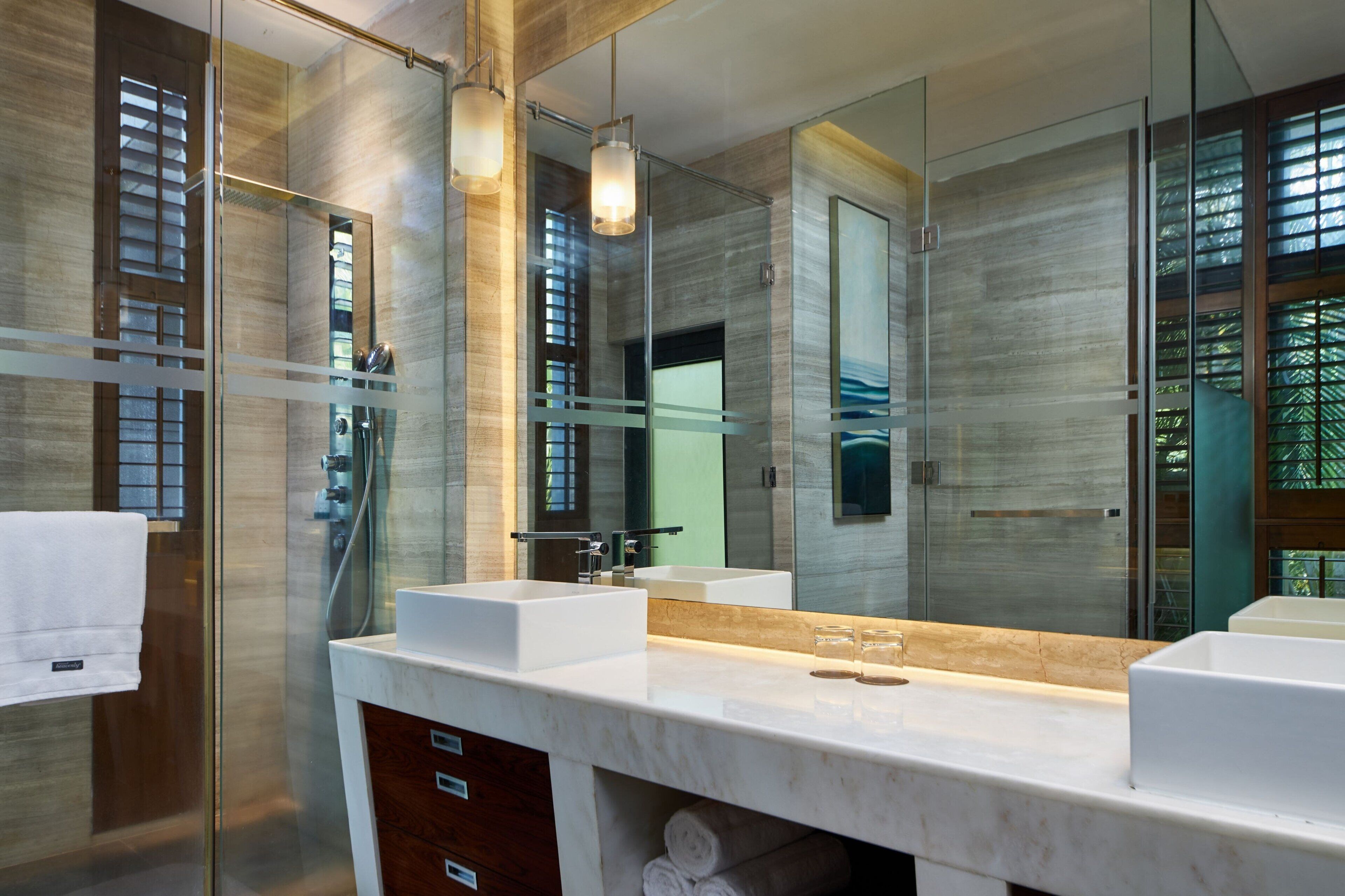 A modern bathroom with a glass shower enclosure, a large mirror, and a marble countertop.