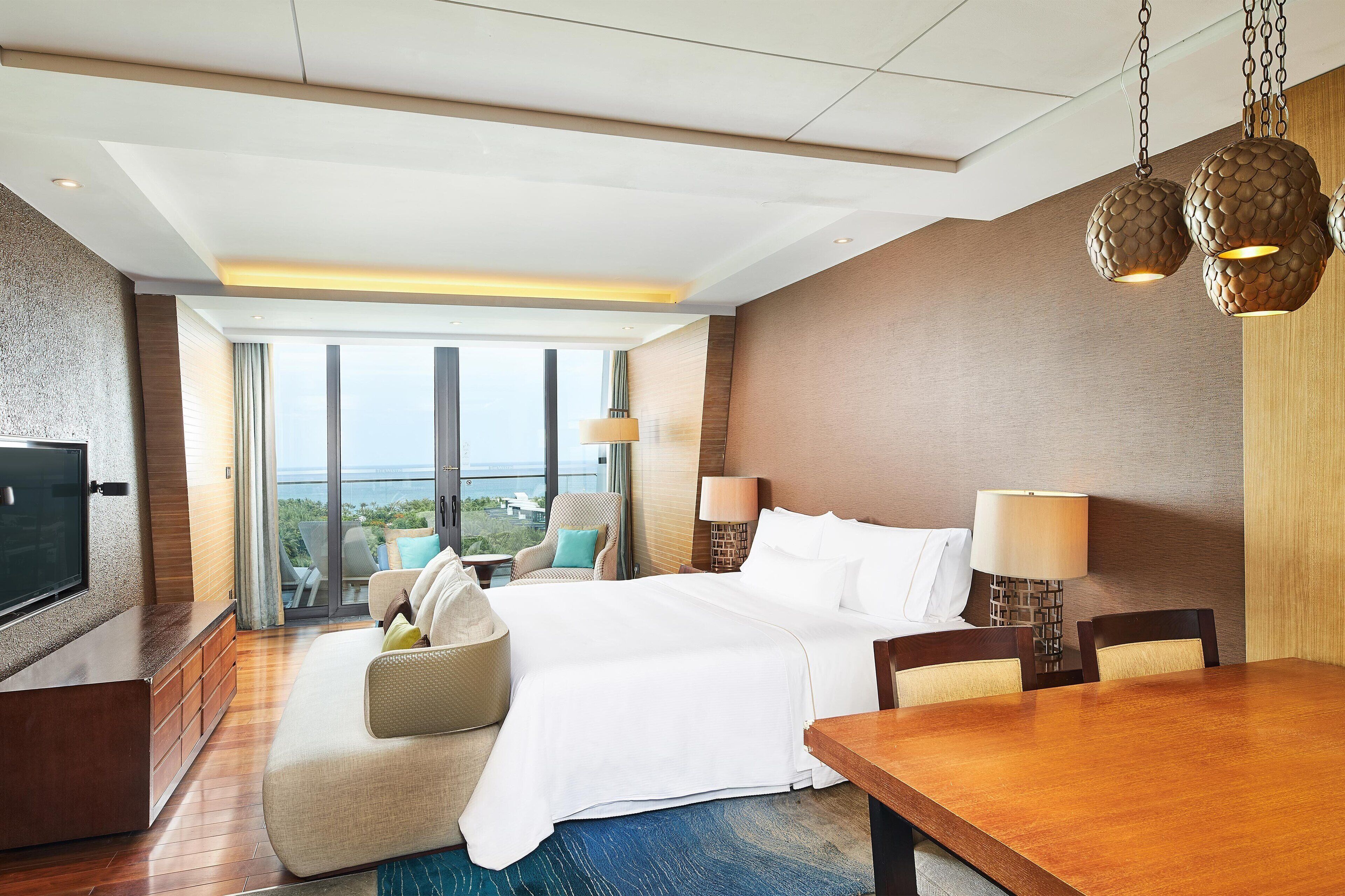 A hotel room with a bed, a TV, a dining table, and a view of the outdoors.