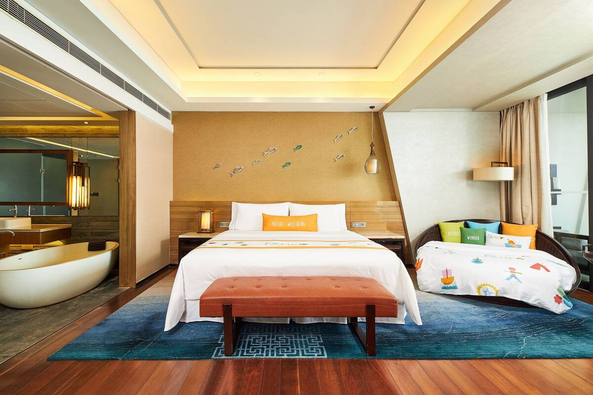 Une chambre d’hôtel avec un lit, un banc, une baignoire et une grande fenêtre.