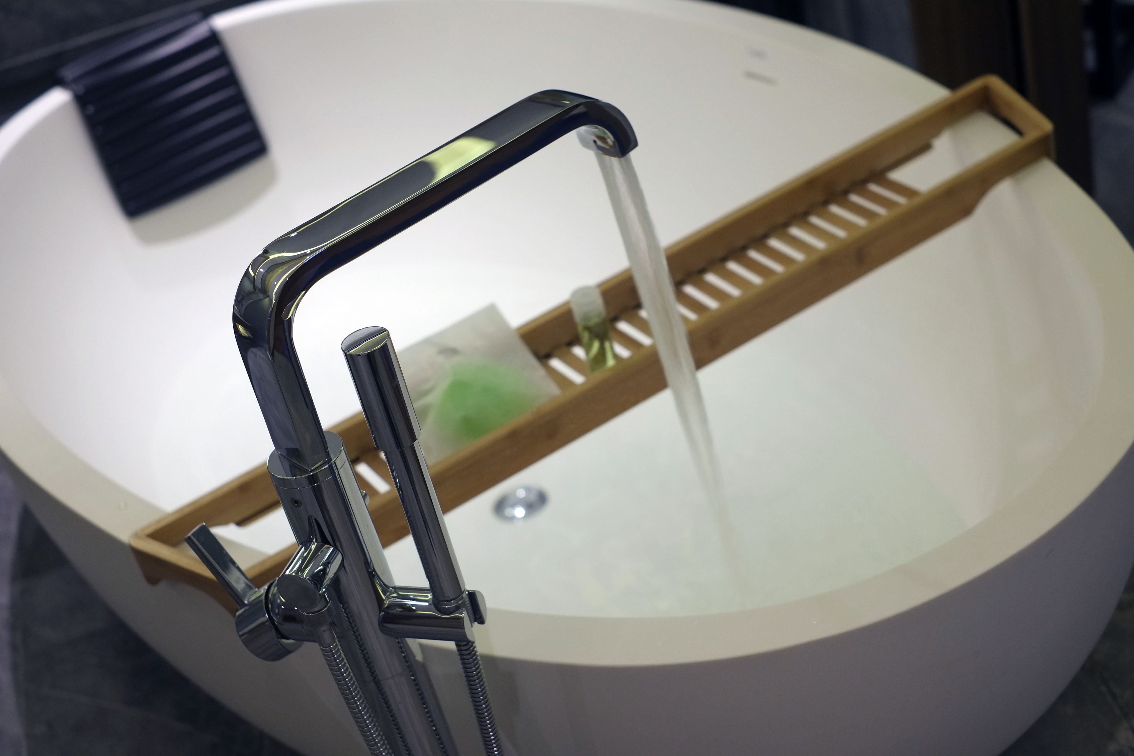 A modern bathroom with a large bathtub, a handheld showerhead, and a wooden bath tray.