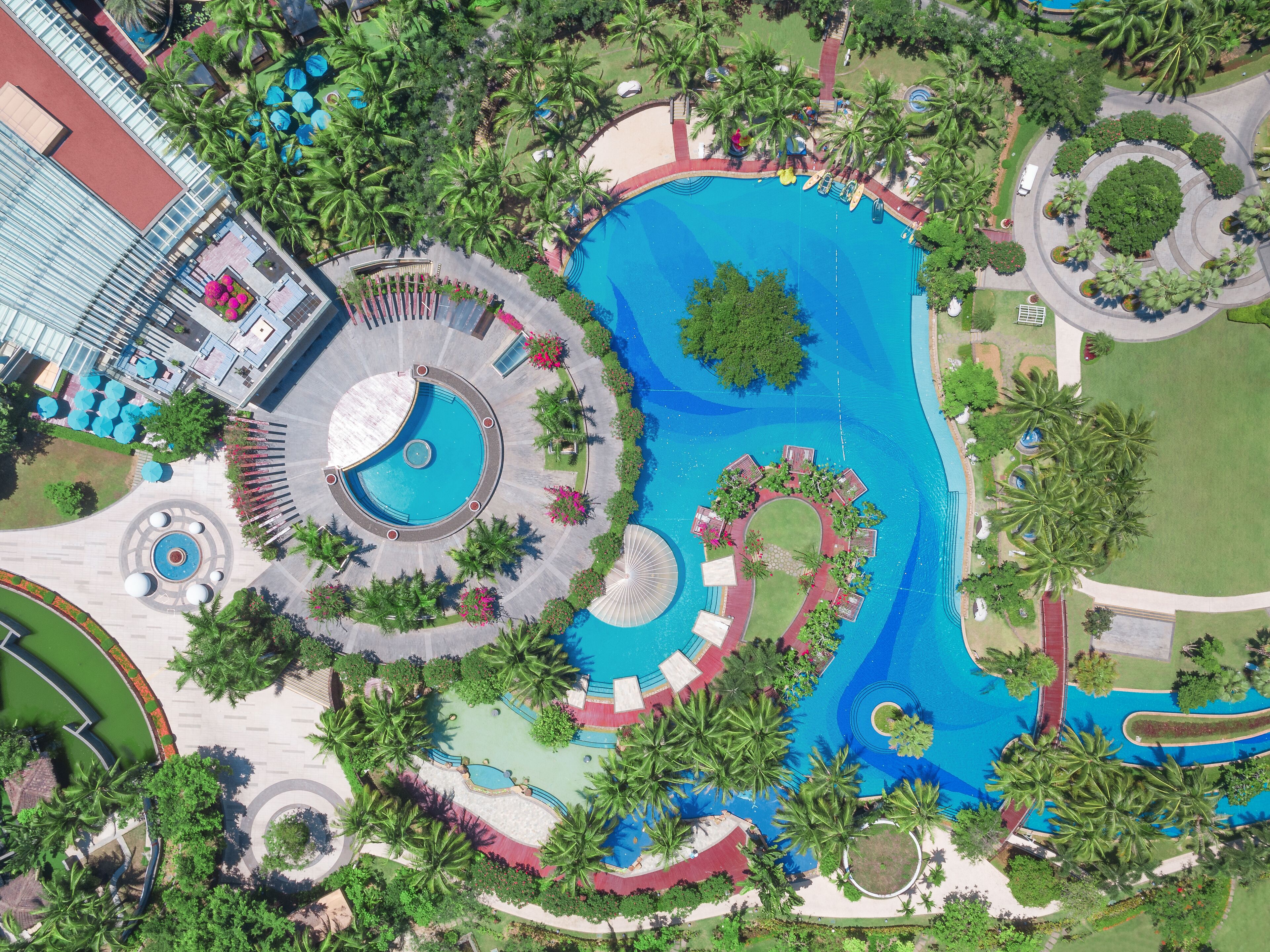 Une grande piscine circulaire agrémentée de plusieurs jeux d’eau, entourée de palmiers et d’un jardin bien entretenu.