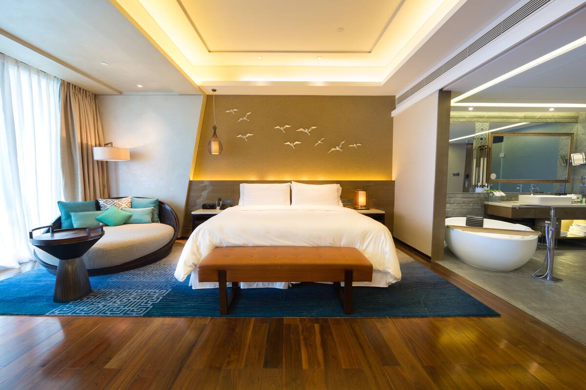 Une chambre d’hôtel moderne dotée d’un grand lit, d’un coin salon circulaire, d’une baignoire et d’un grand miroir.