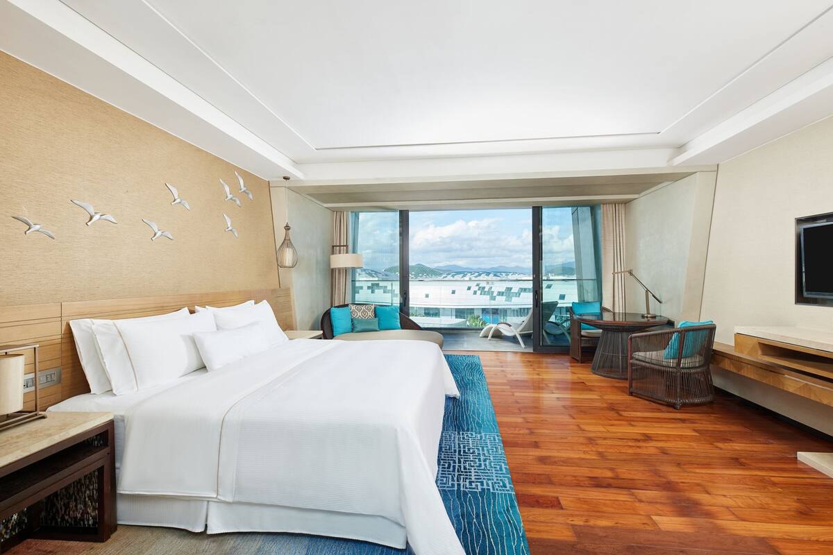 Une chambre d’hôtel avec un grand lit, un coin salon avec des fauteuils, une télévision et une vue sur la ville.
