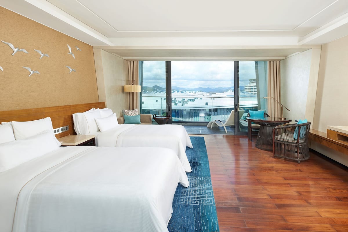 Une chambre d’hôtel avec deux lits, une vue sur la ville, un balcon et un coin salon avec une table et des chaises.