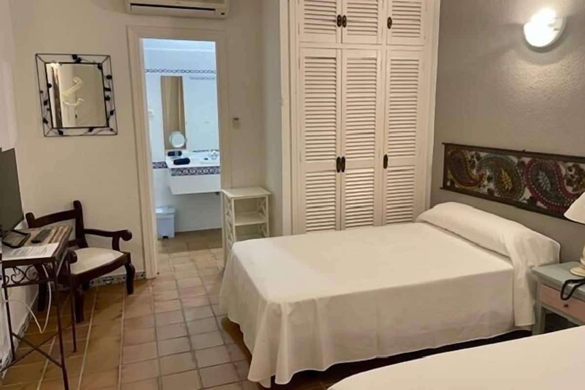 A hotel room with a bed, a desk, a chair, a wardrobe, and a bathroom visible through an open door.