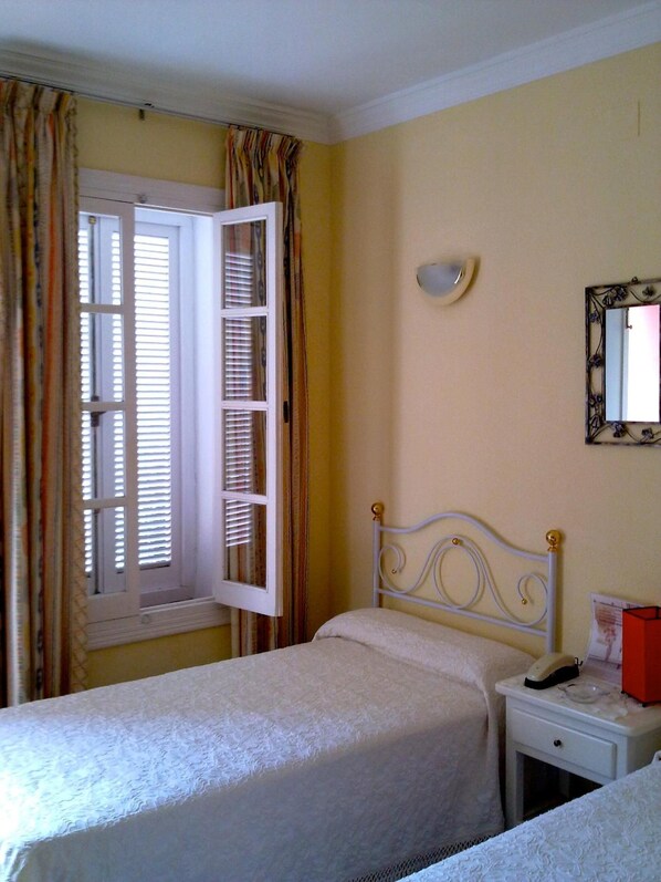 A bedroom with two beds, a window with open shutters, a bedside table with a lamp, and a wall-mounted mirror. - Hotel La Peña (Tarifa)