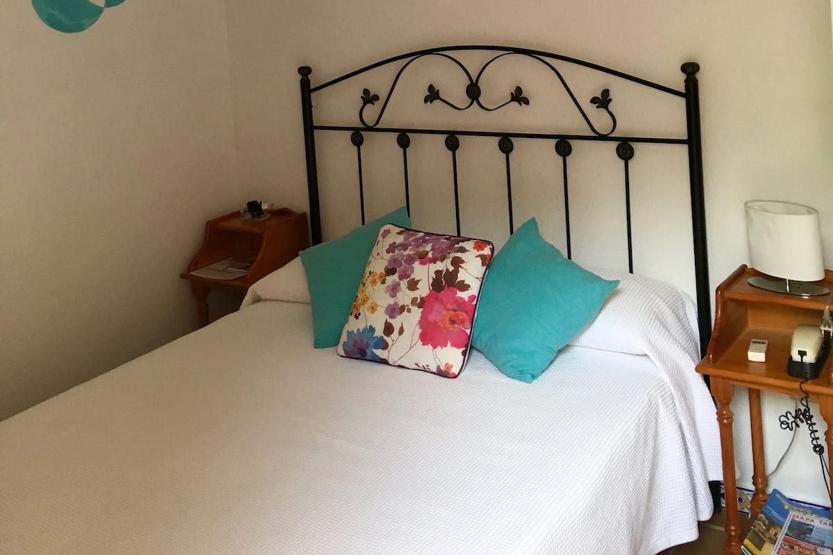 A neatly made bed with a floral pillow, a bedside table with a lamp, and two wall-mounted paintings.