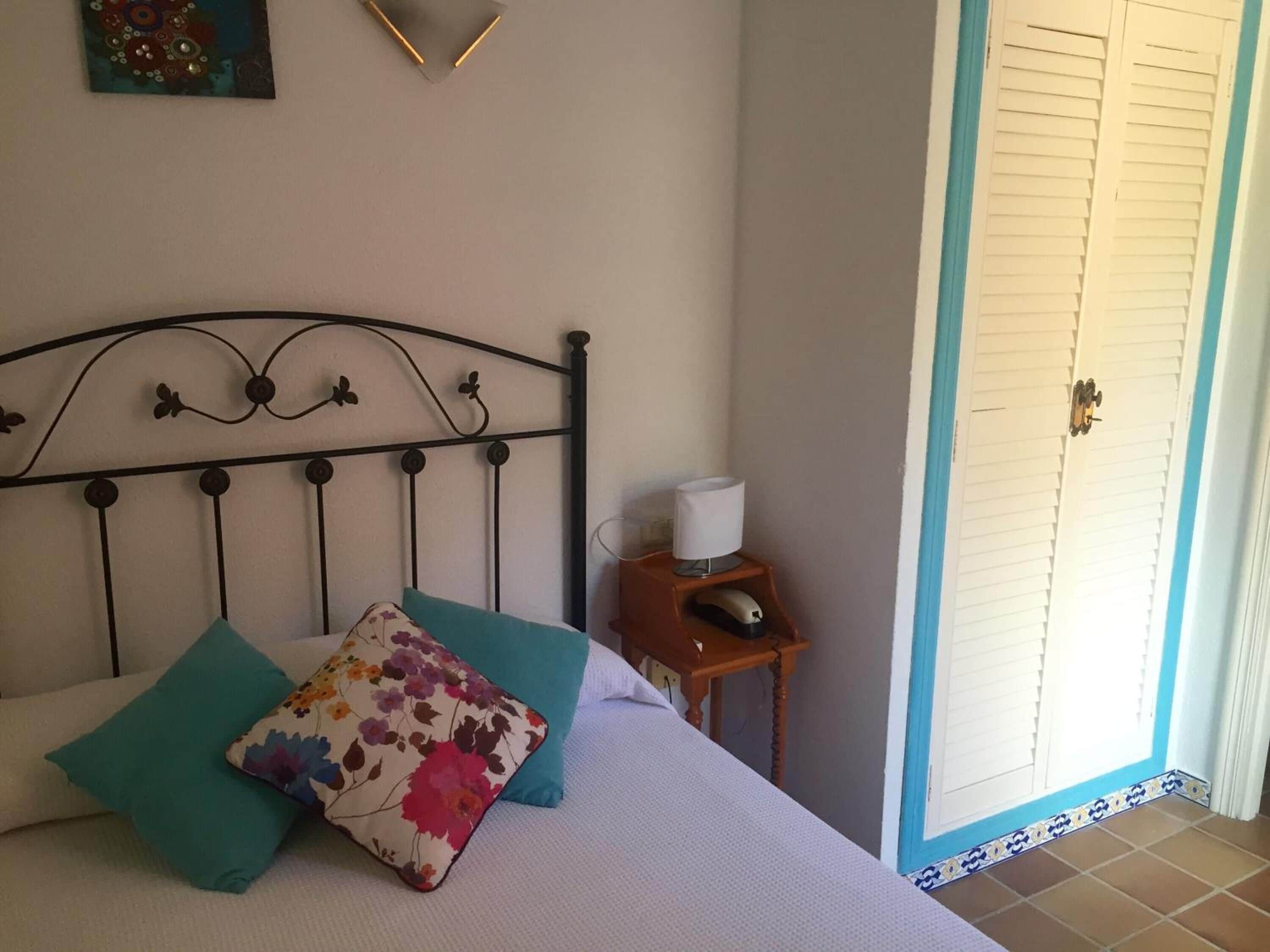 Une chambre à coucher avec un lit, des oreillers, une table de chevet avec une lampe et une porte.