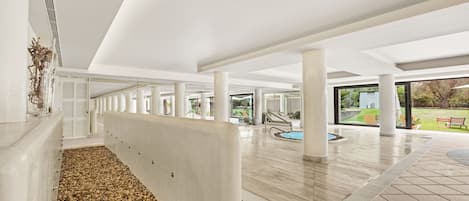 A spacious indoor area with a pebble-lined walkway, large pillars, and a view of an outdoor garden.