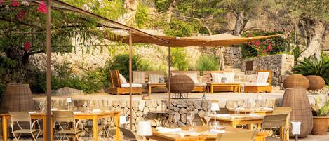 Un espace de restauration en plein air avec des murs en pierre, du mobilier en bois et un coin salon ombragé.