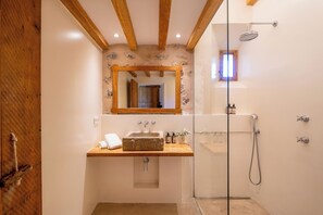 A bathroom with a wooden beam ceiling, a stone sink, a glass shower enclosure, and a mirror with a wooden frame.