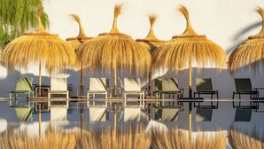 A pool area with thatched umbrellas and lounge chairs. - Hotel Es Port (Sóller)