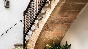 A stone staircase with a metal railing, leading to an upper floor. There are potted plants at the base of the stairs.