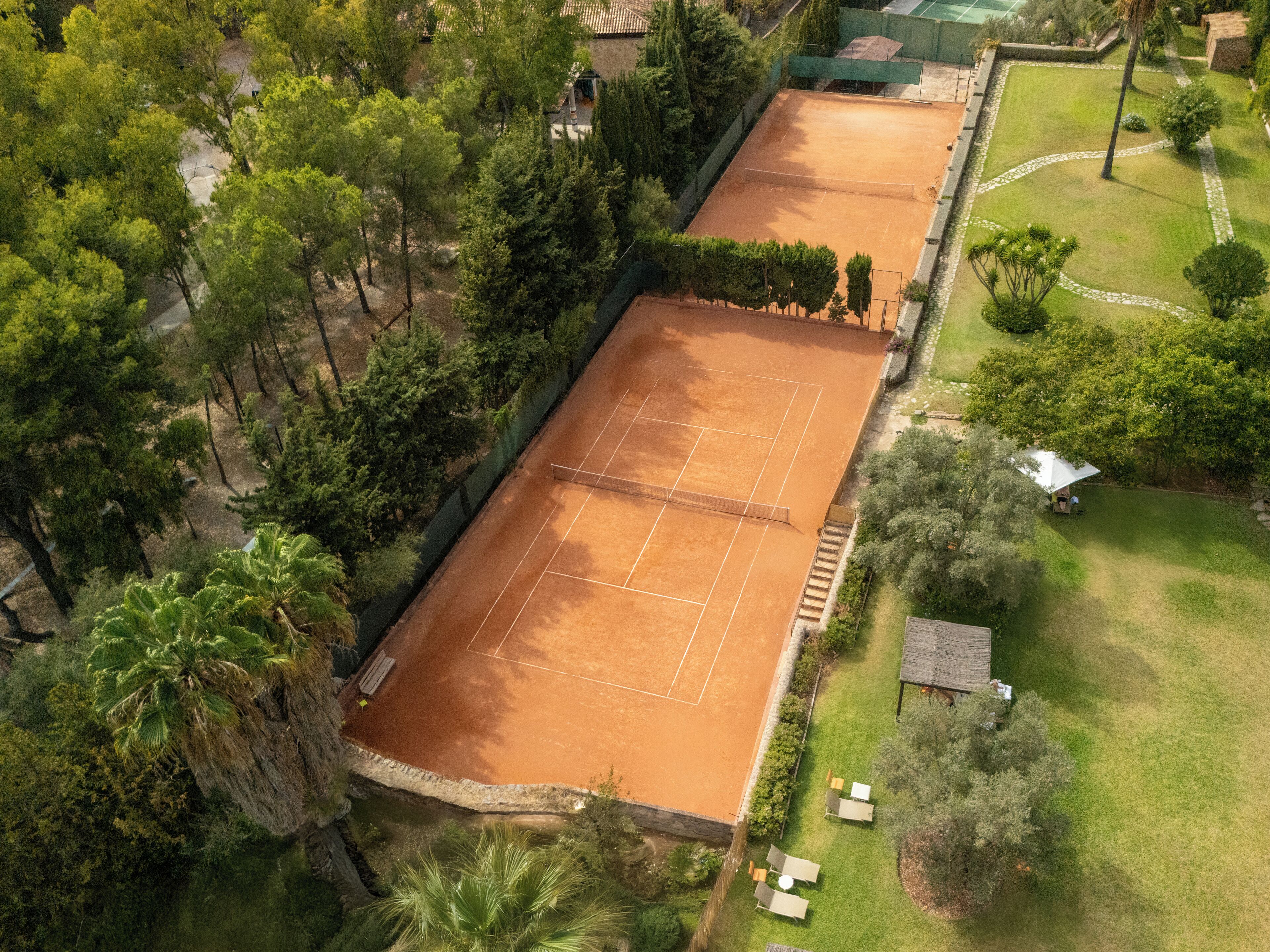 Luftaufnahme eines Tennisplatzes, umgeben von Bäumen und einem kleinen Gebäude.