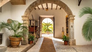 An arched corridor with a central rug, potted plants, and a view of a garden. - Hotel Es Port (Sóller)