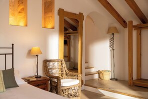 A bedroom with a bed, a wicker chair, a bedside table with a lamp, a wooden wardrobe, and a floor lamp.