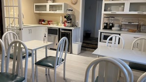 A modern kitchen with white cabinetry, a dining area with white chairs, and a small refrigerator.