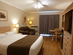 A hotel room with a bed, a desk, a chair, a television, and a ceiling fan. - Motel Becancour (Becancour)