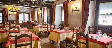 A restaurant with multiple tables set for dining, featuring wooden chairs and red and yellow tablecloths.