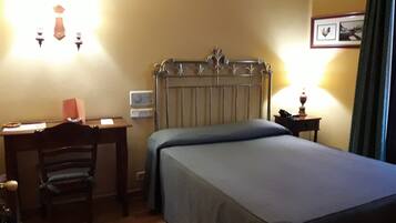 Una habitación de hotel con cama, escritorio, silla, radiador y lámpara.