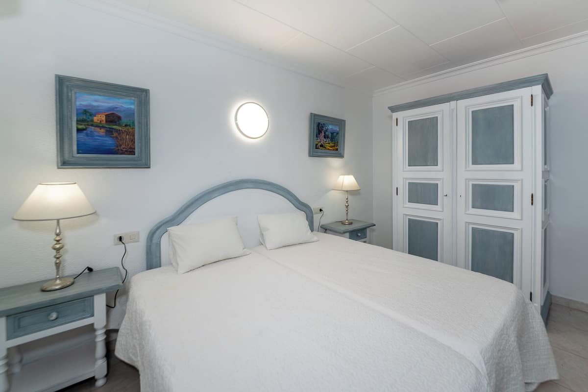 Une chambre à coucher comprenant un lit, deux tables de chevet, deux lampes fixées au mur et deux tableaux encadrés.
