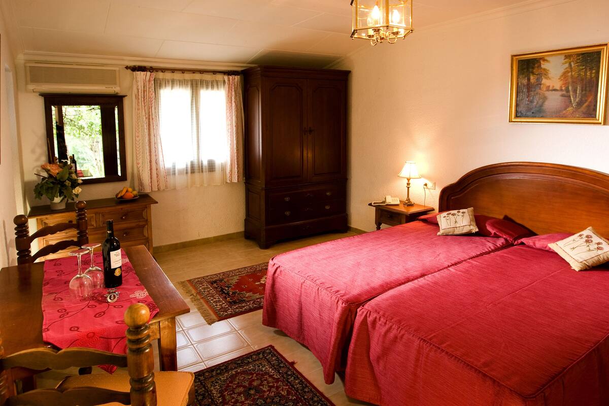 Une chambre avec deux lits, une commode en bois, une table à manger avec des chaises et une fenêtre avec des rideaux.