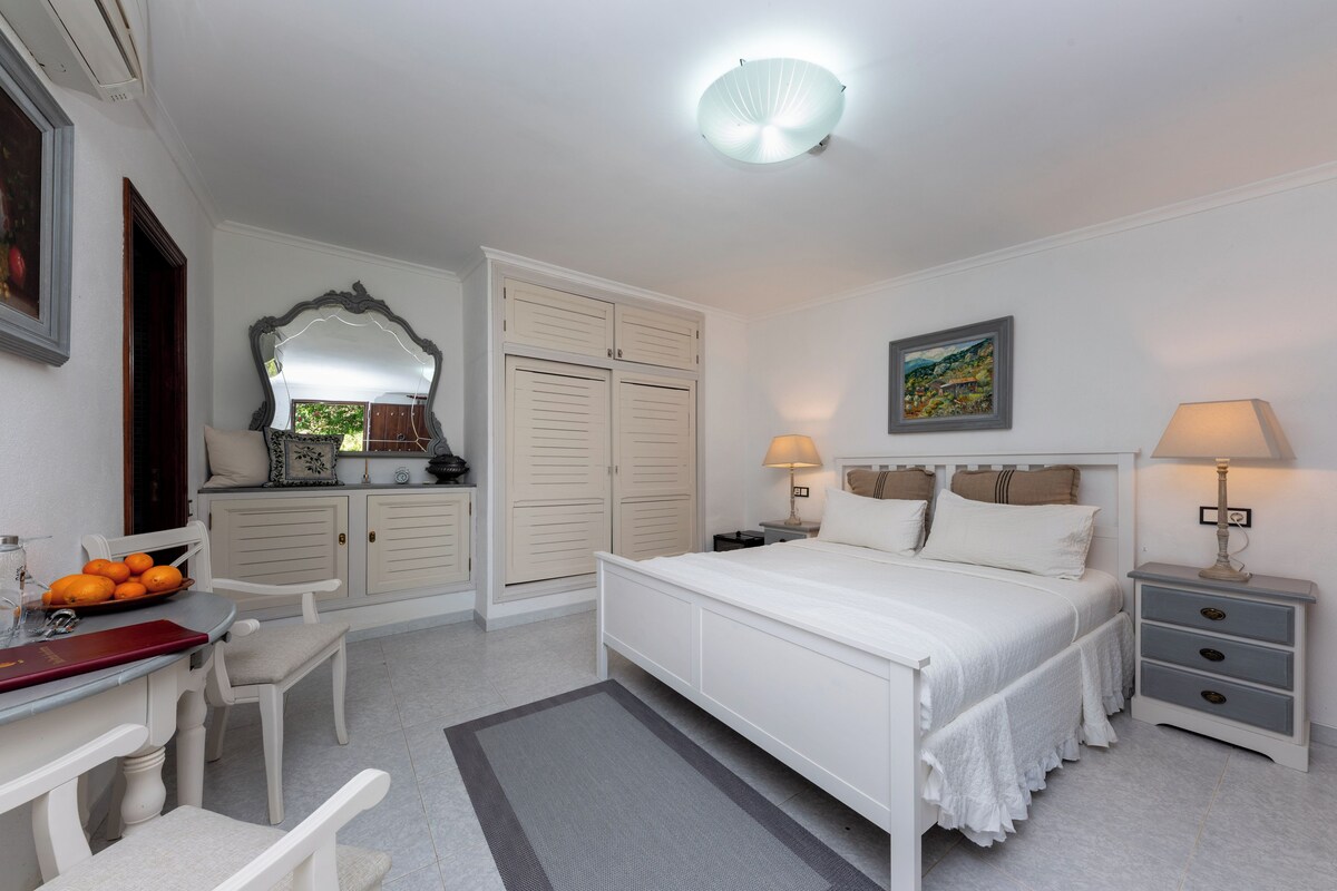 Un dormitorio con cama, mesitas de noche, escritorio, silla, armario y espejo.