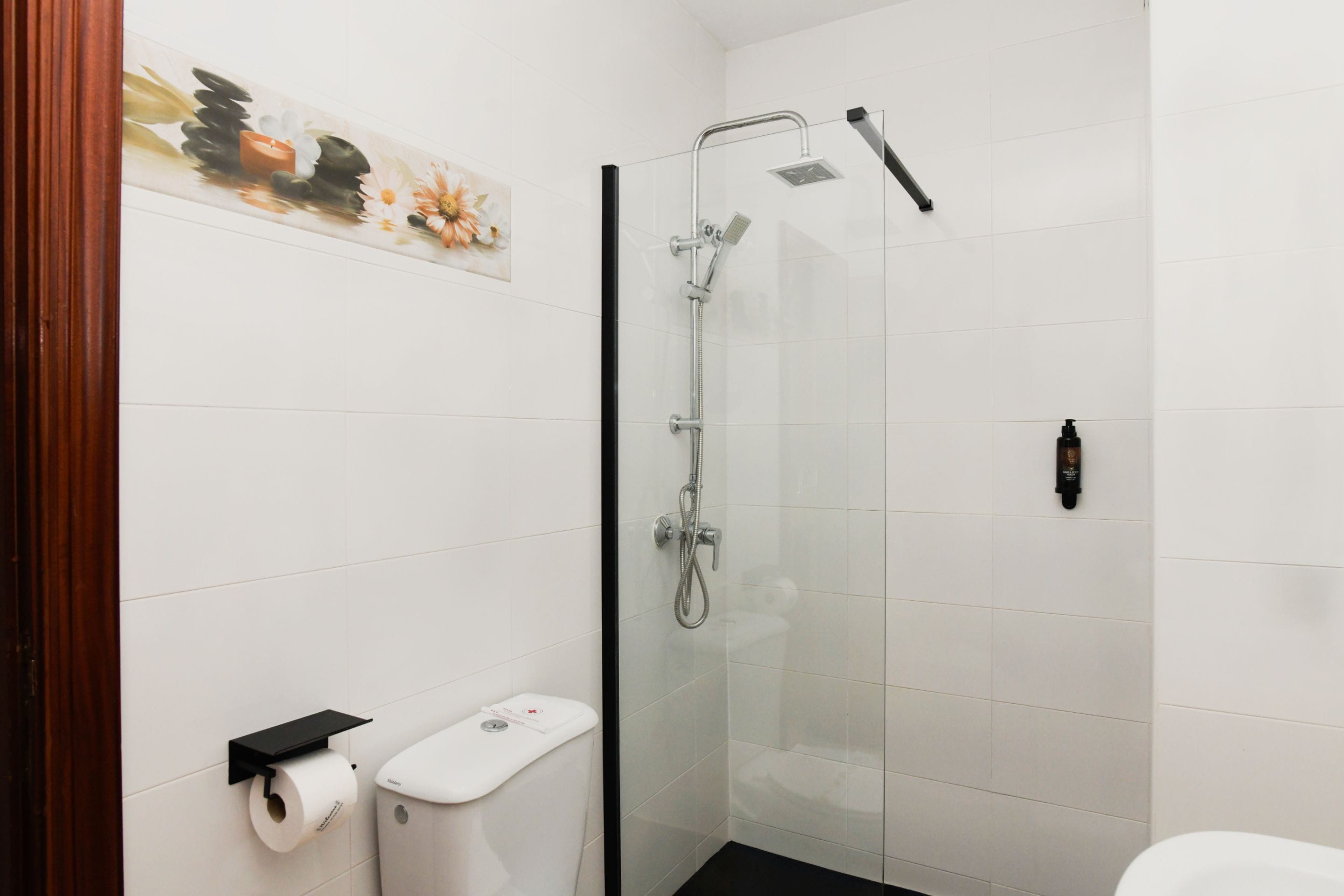 Un baño moderno con ducha envuelta en vidrio, inodoro con dispensador de toallas de papel y jabonera de pared.