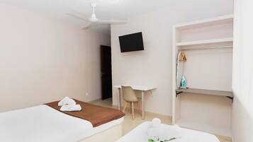 A hotel room with two beds, a desk, a chair, a TV, and a shelf with clothes and an iron.