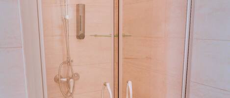 A glass-enclosed shower stall with a handheld showerhead, a handheld shower head, and a wall-mounted faucet.