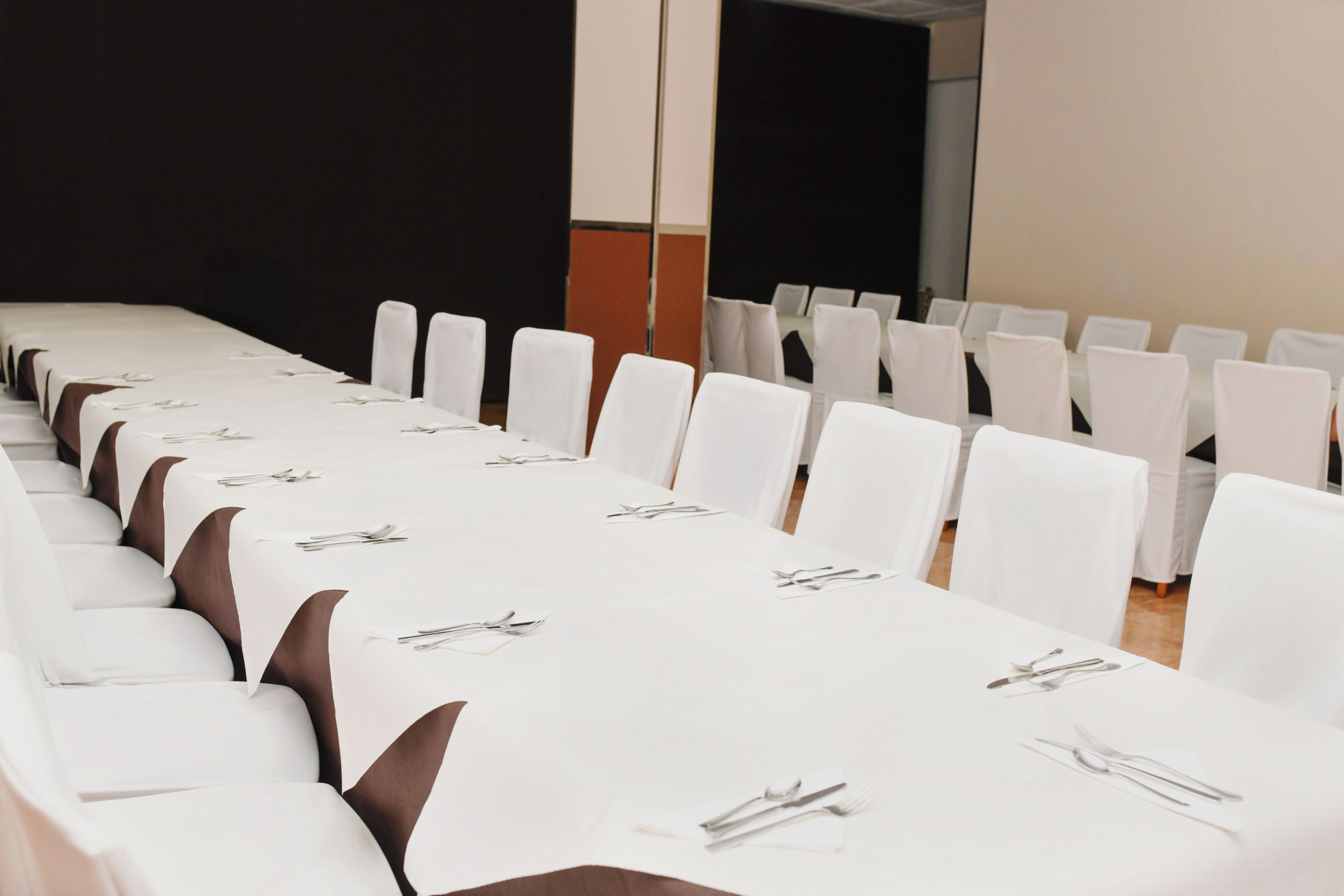 Un salón de conferencias con filas de mesas y sillas blancas, cada conjunto con cubiertos.