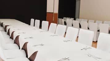 Un salón de conferencias con filas de mesas y sillas blancas, cada conjunto con cubiertos.