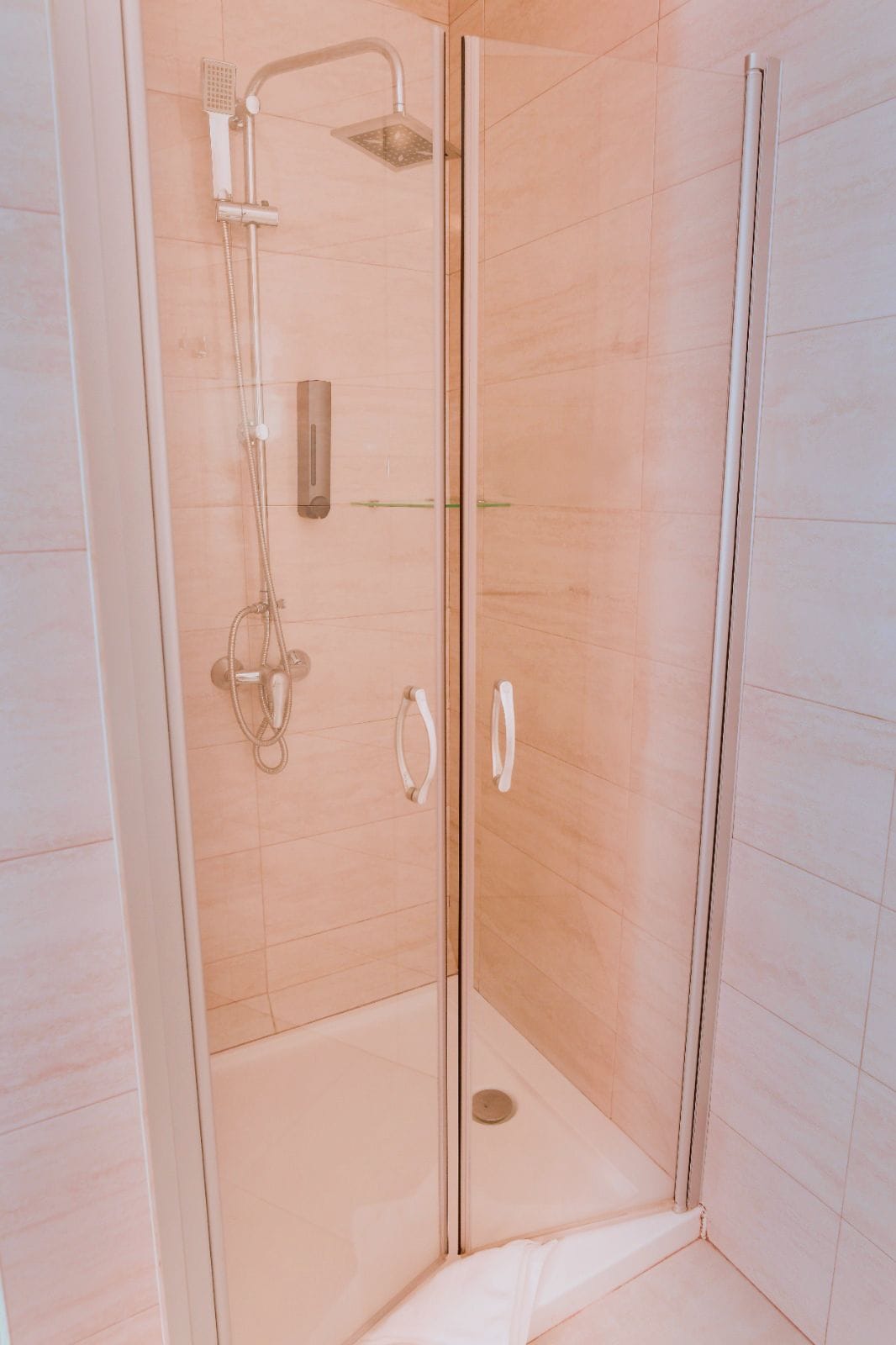 Ducha envuelta en vidrio con cabezal de ducha manual y llave de pared.