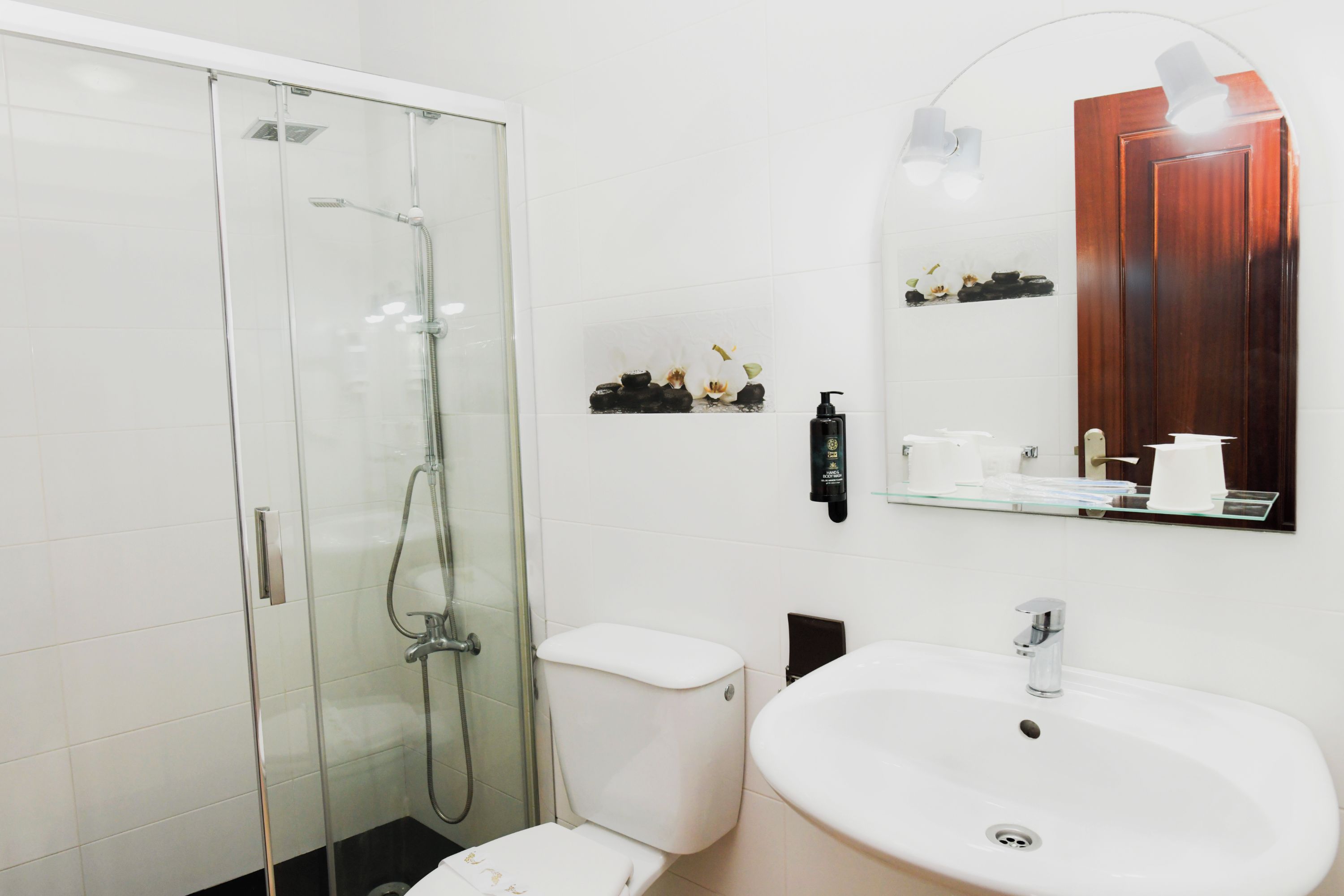 A modern bathroom with a glass-enclosed shower, a white toilet, a sink with a mirror above it, and a wooden cabinet with toiletries.