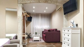 Una habitación funcional con sofá, televisor, cómoda y una mesita.