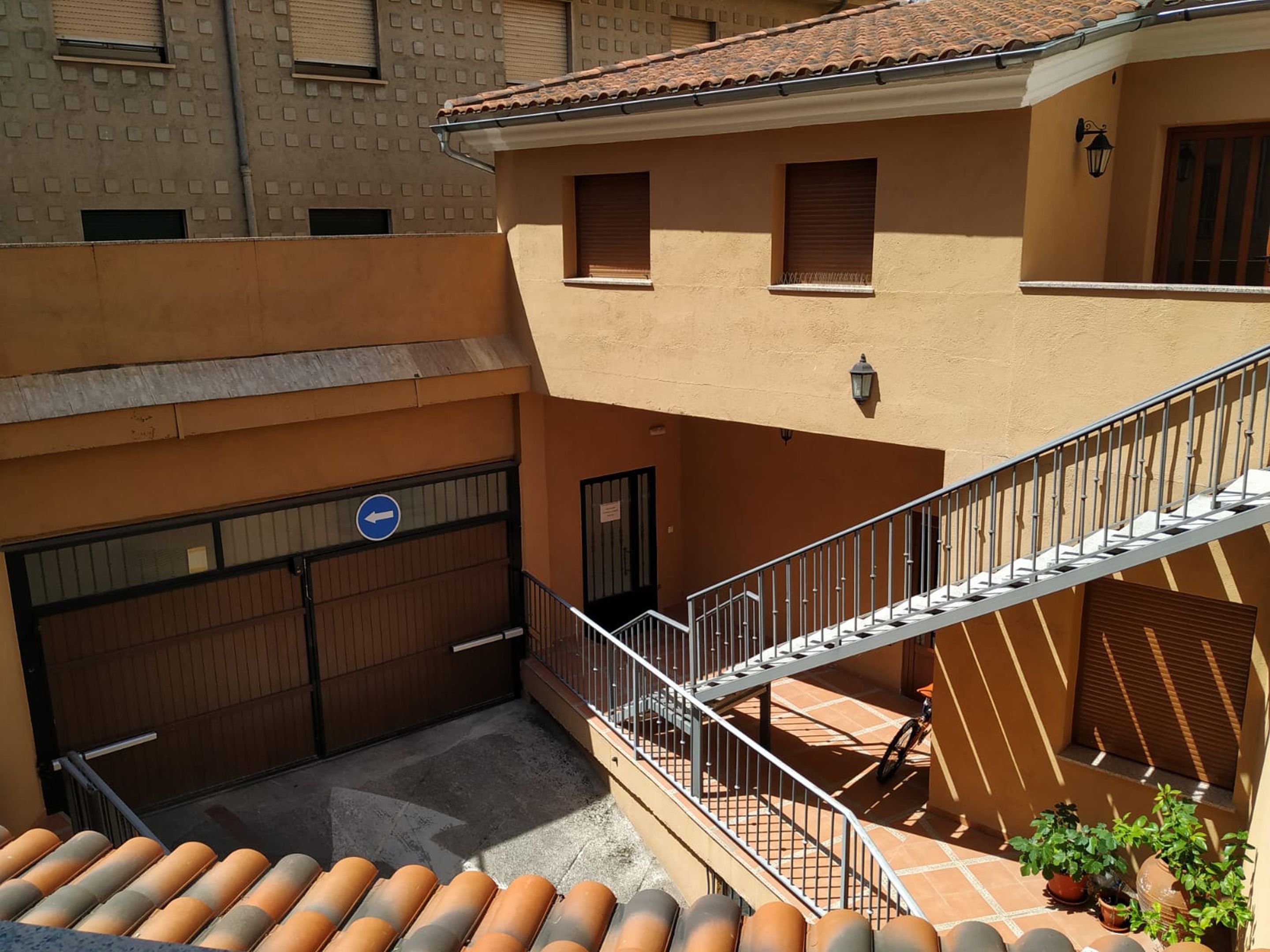 A courtyard with a staircase leading to an upper level, a gated entrance, and potted plants.