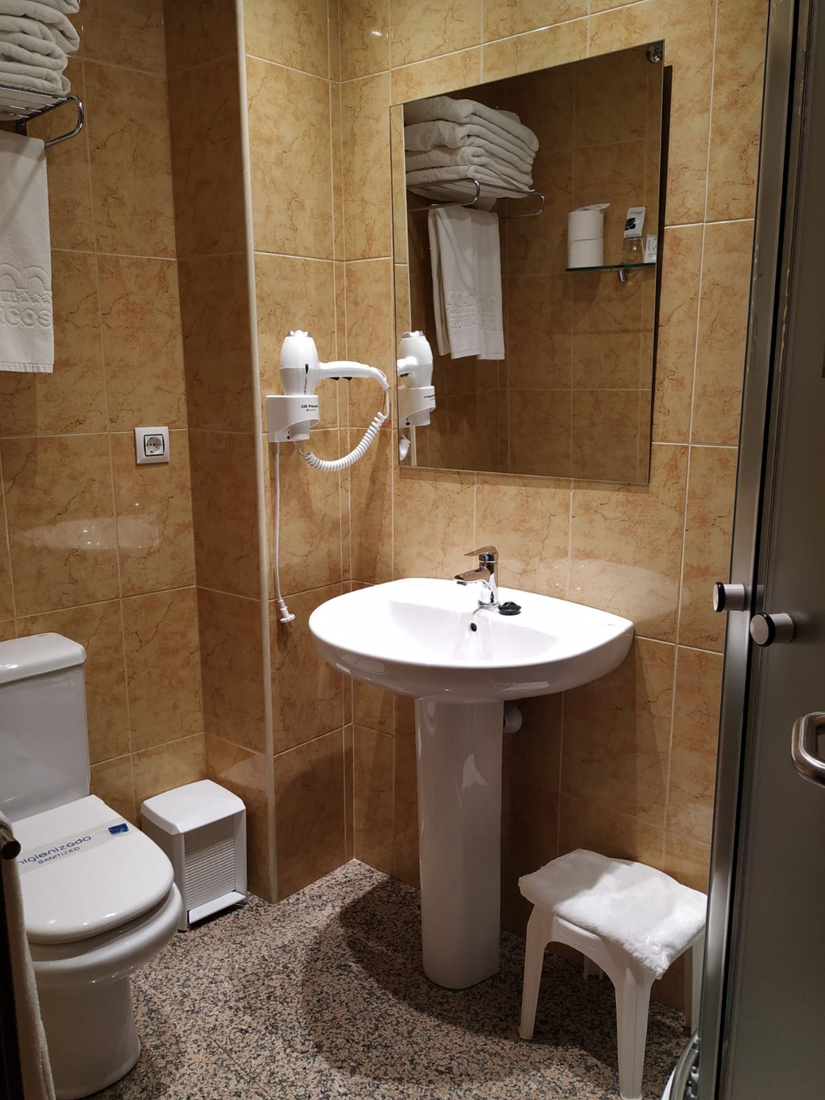 A bathroom with a white sink, two hair dryers, a toilet, and a small stool.