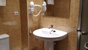 A bathroom with a white sink, two hair dryers, a toilet, and a small stool.
