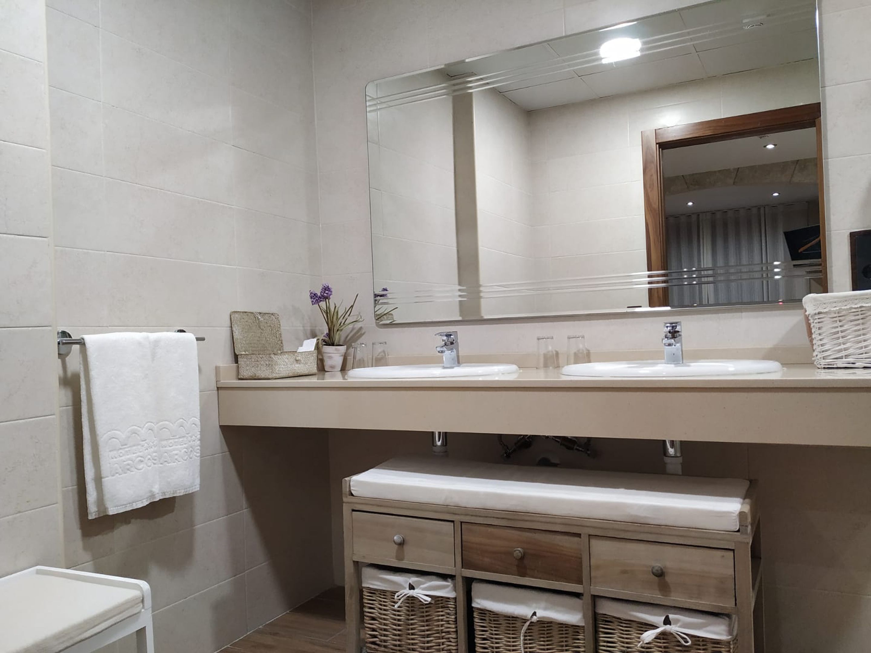 A bathroom with two sinks, a mirror, a towel rack, and wicker baskets under the counter.